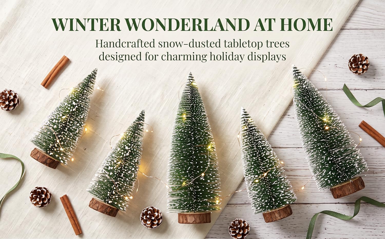 Text reads 'WINTER WONDERLAND AT HOME' and 'Handcrafted snow-dusted miniature trees designed for charming holiday displays.' Flat lay of five small evergreen trees with snow coating, pinecones, cinnamon sticks, and holiday decorations on white background.